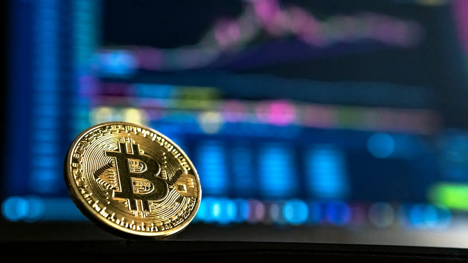 Gold bitcoin coin in front of a trading screen