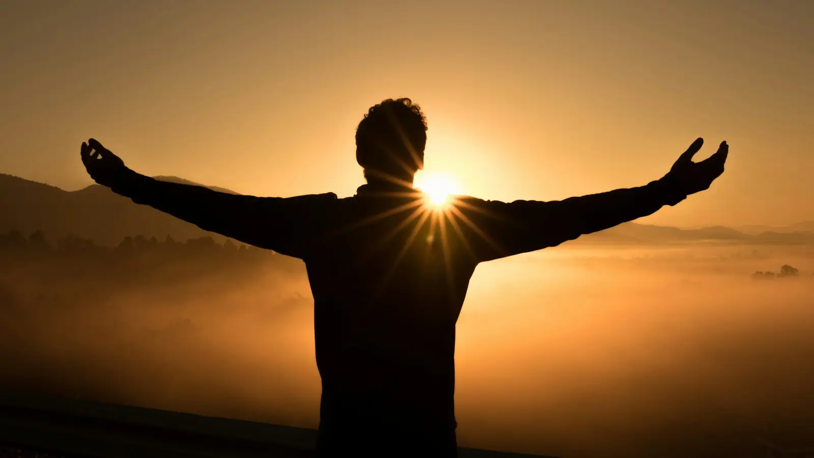 Person with arms outstretched facing the sunrise